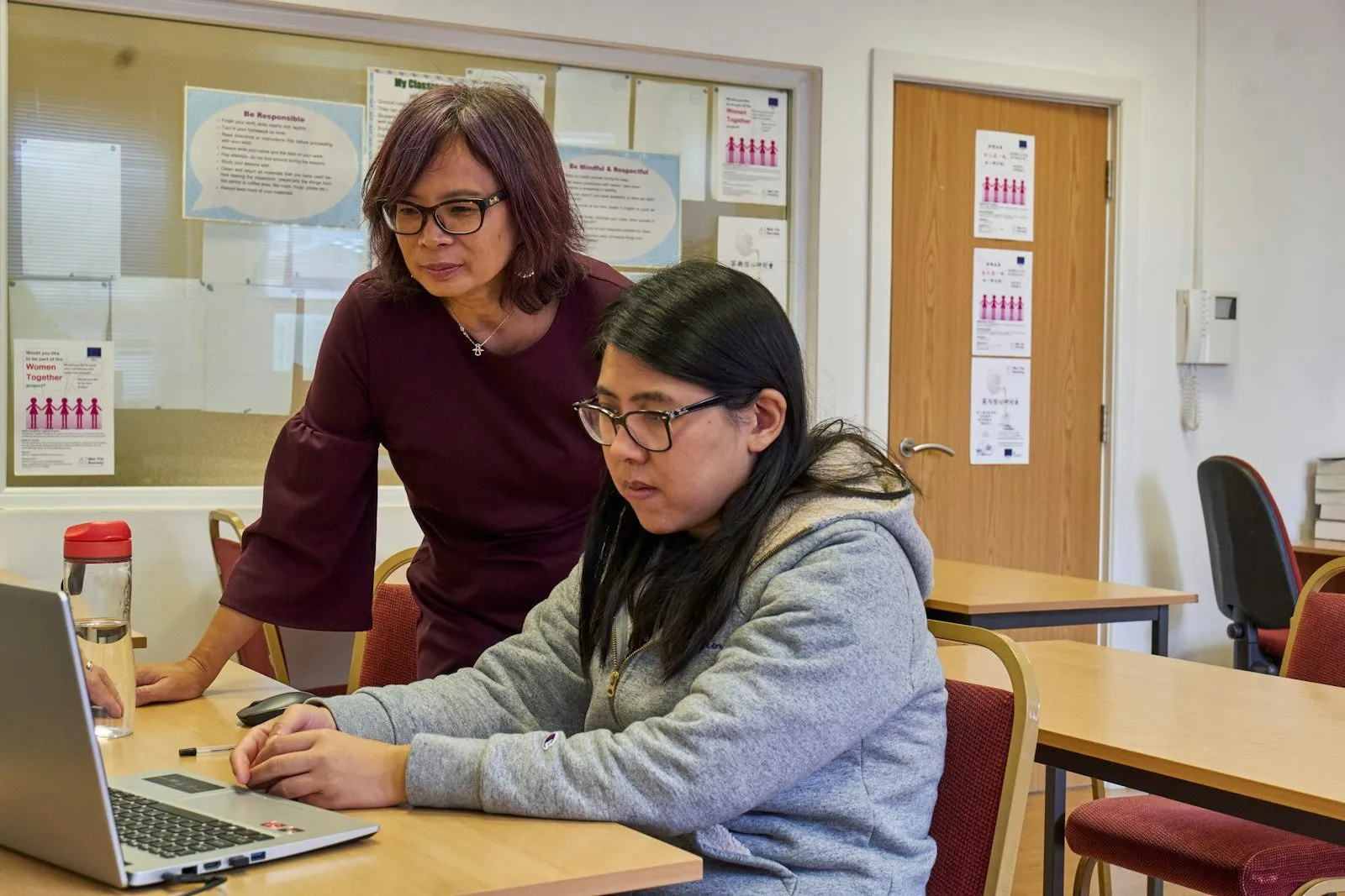 Profesora acompañando a una alumna frente a la computadora